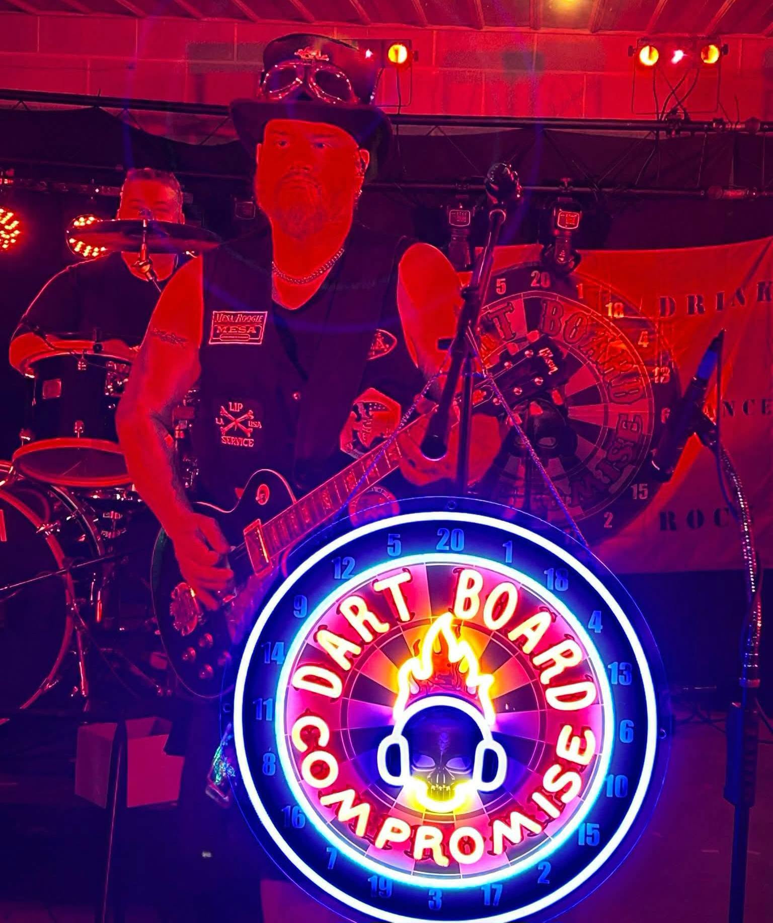 DBC guitarist on stage with the neon Dart Board Compromise sign